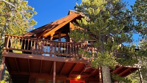 A wooden cabin with a balcony, a red door, and a staircase leading to the entrance.