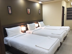 A hotel room with three single beds, each with white linens and a wooden headboard. There are wall-mounted lamps on either side of the beds. - Kans One Madipakkam (Chennai)