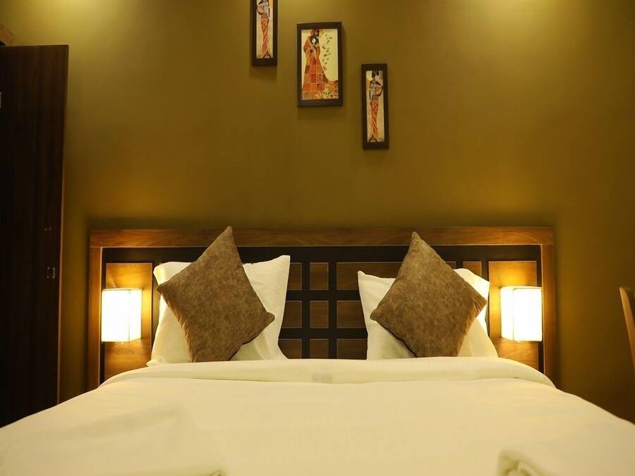 A hotel room with a bed, two wall-mounted lamps, and three framed artworks on the wall.