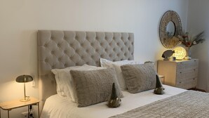 A neatly made bed with a tufted headboard, a bedside lamp, and a small nightstand with a decorative lamp and vase. -  Beautiful charming flat, beautiful terrace facing the sea. Exceptional location (Albufeira)