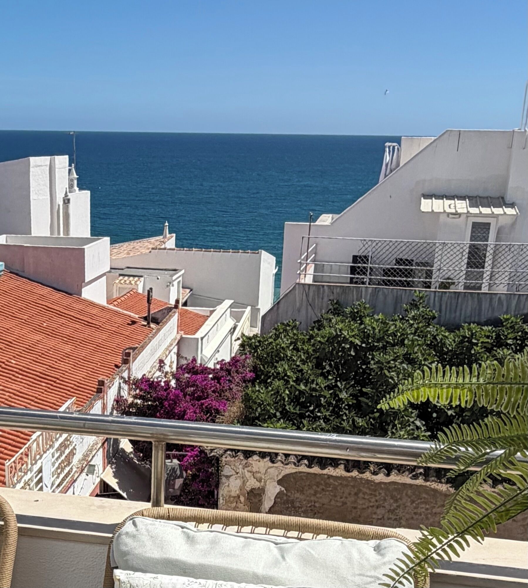 A coastal building with a view of the sea, a balcony with a railing, and a small garden area.