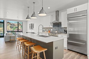 Une cuisine moderne dotée d’un grand îlot central, d’appareils électroménagers en acier inoxydable et de tabourets de bar.