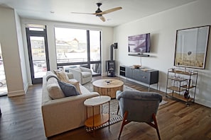A modern living room with a sofa, armchairs, a coffee table, a TV, a fireplace, and a balcony with a view of buildings.