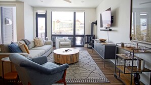 A modern living room with a sofa, armchair, and coffee table. There is a TV mounted on the wall and a fireplace. - Urban Luxury - Rooftop Patio w/ Hot Tub, Perfect for 2 Families at Competitive Rates (Steamboat Springs)