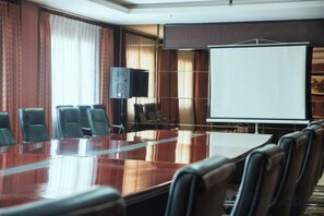 Un salón de conferencias con una larga mesa, varias sillas, una pantalla de proyector y un orador.