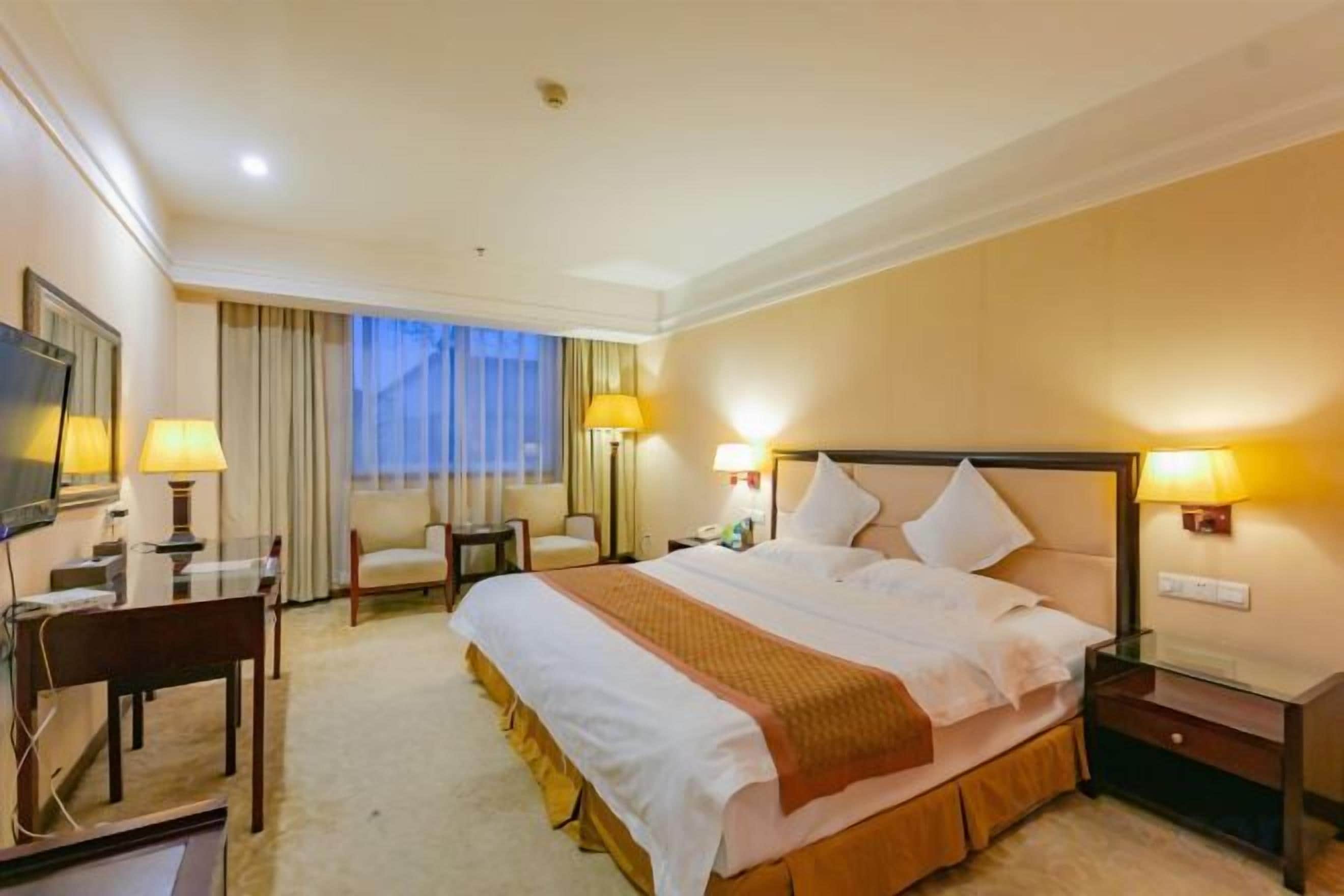 A hotel room with a large bed, two bedside tables, a desk with a chair, and a television.