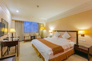 A hotel room with a large bed, two bedside tables, a desk with a chair, and a television.