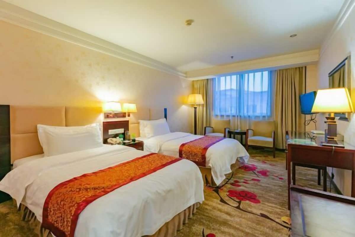 Une chambre d’hôtel avec deux lits, un bureau, une chaise, une télévision et une fenêtre avec des rideaux.