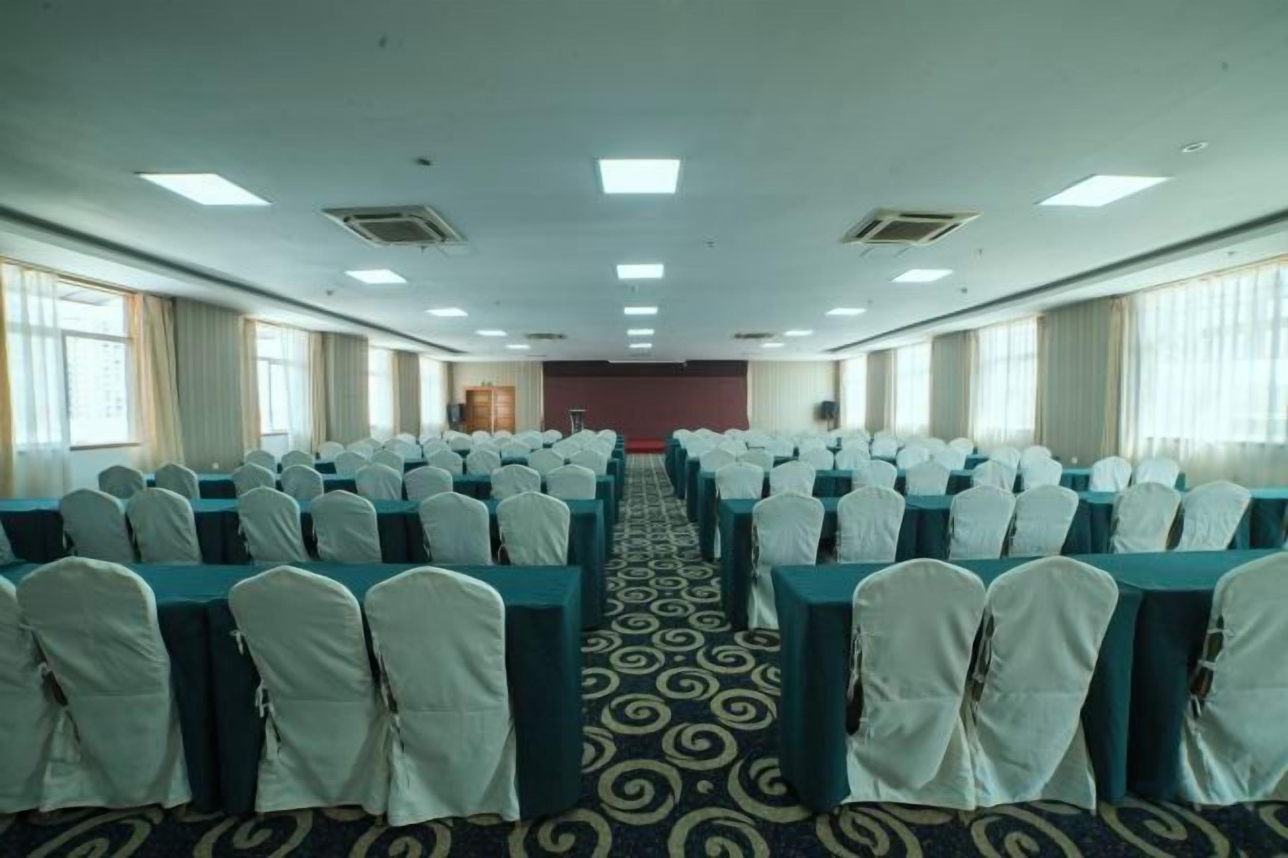 A conference room with rows of tables and chairs, a carpeted floor, and large windows on one side.