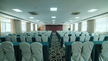 A conference room with rows of tables and chairs, a carpeted floor, and large windows on one side.