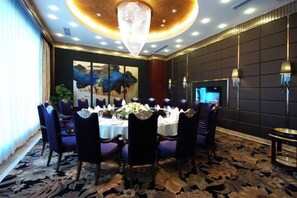 A dining area with a round table set for six, surrounded by chairs, in a room with a large painting on the wall and a chandelier. - Xin Shun Hotel (Hongya)