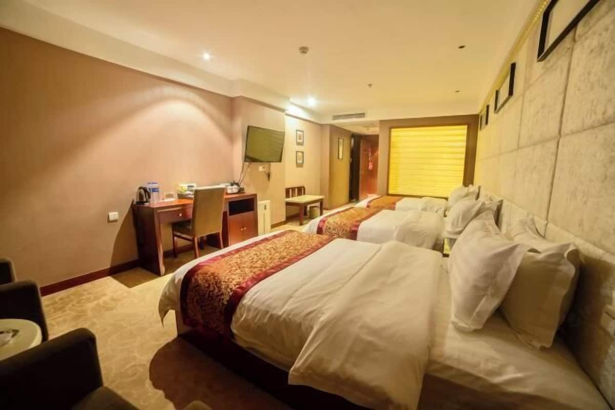 Une chambre d’hôtel avec deux lits, un bureau, une chaise, une télévision et une fenêtre avec des stores.
