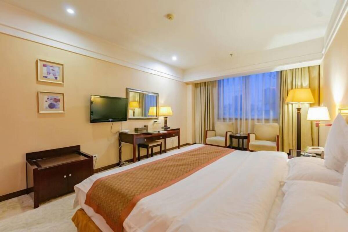 Une chambre d’hôtel avec un grand lit, un bureau, une chaise, une télévision et une fenêtre avec des rideaux.