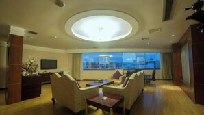 Una habitación de hotel moderna con un ventanal grande, televisor de pantalla plana, un conjunto de sofás y suelo de madera.