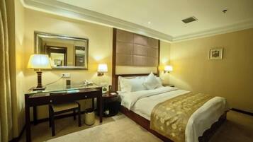 A hotel room with a bed, a desk, a chair, a mirror, and two bedside lamps.
