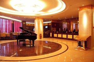 Un lobby amplio con un piano de cola, una recepción y una gran araña.