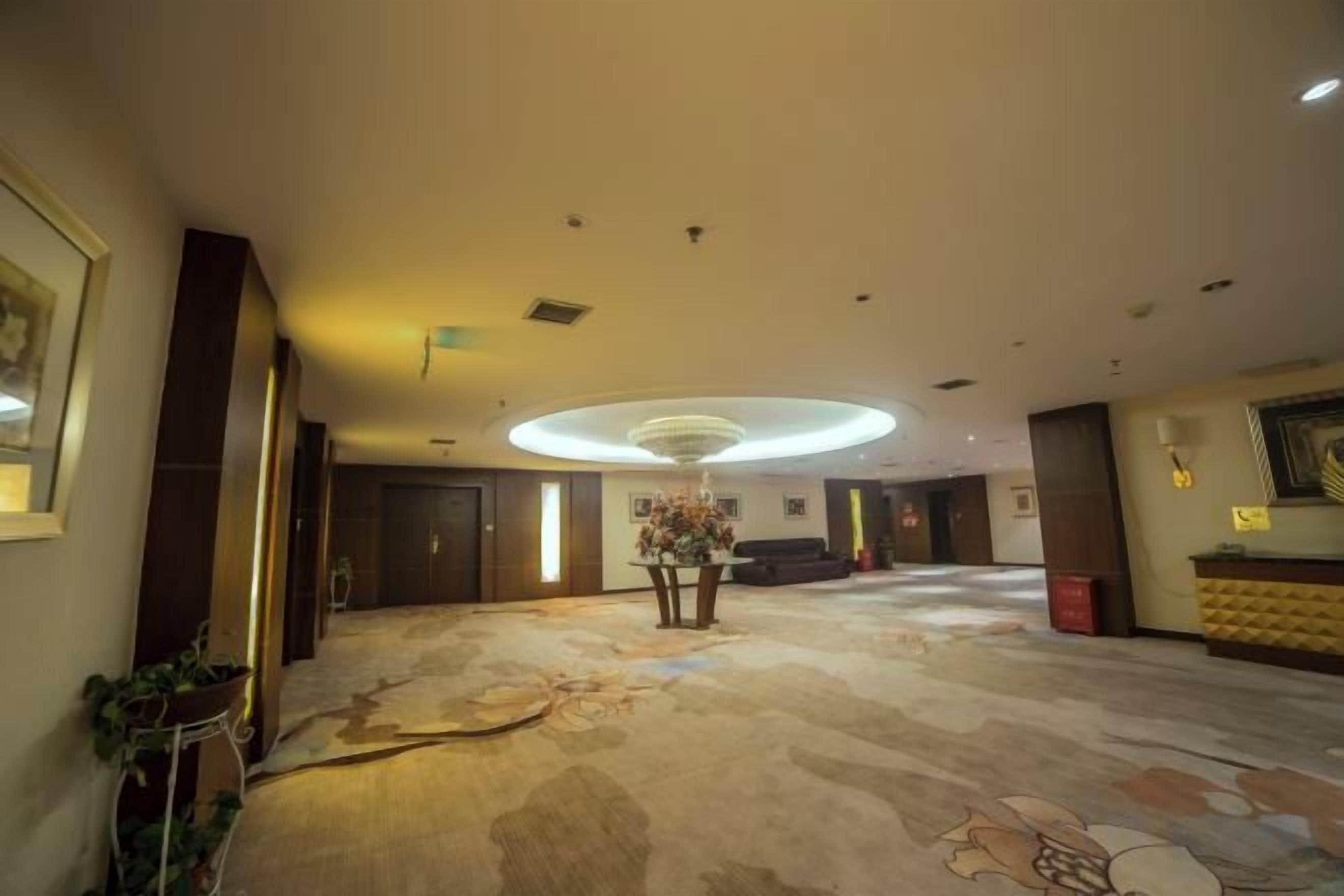 A hotel lobby with a large carpeted area, a reception desk, and a chandelier.