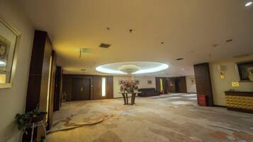 A hotel lobby with a large carpeted area, a reception desk, and a chandelier.