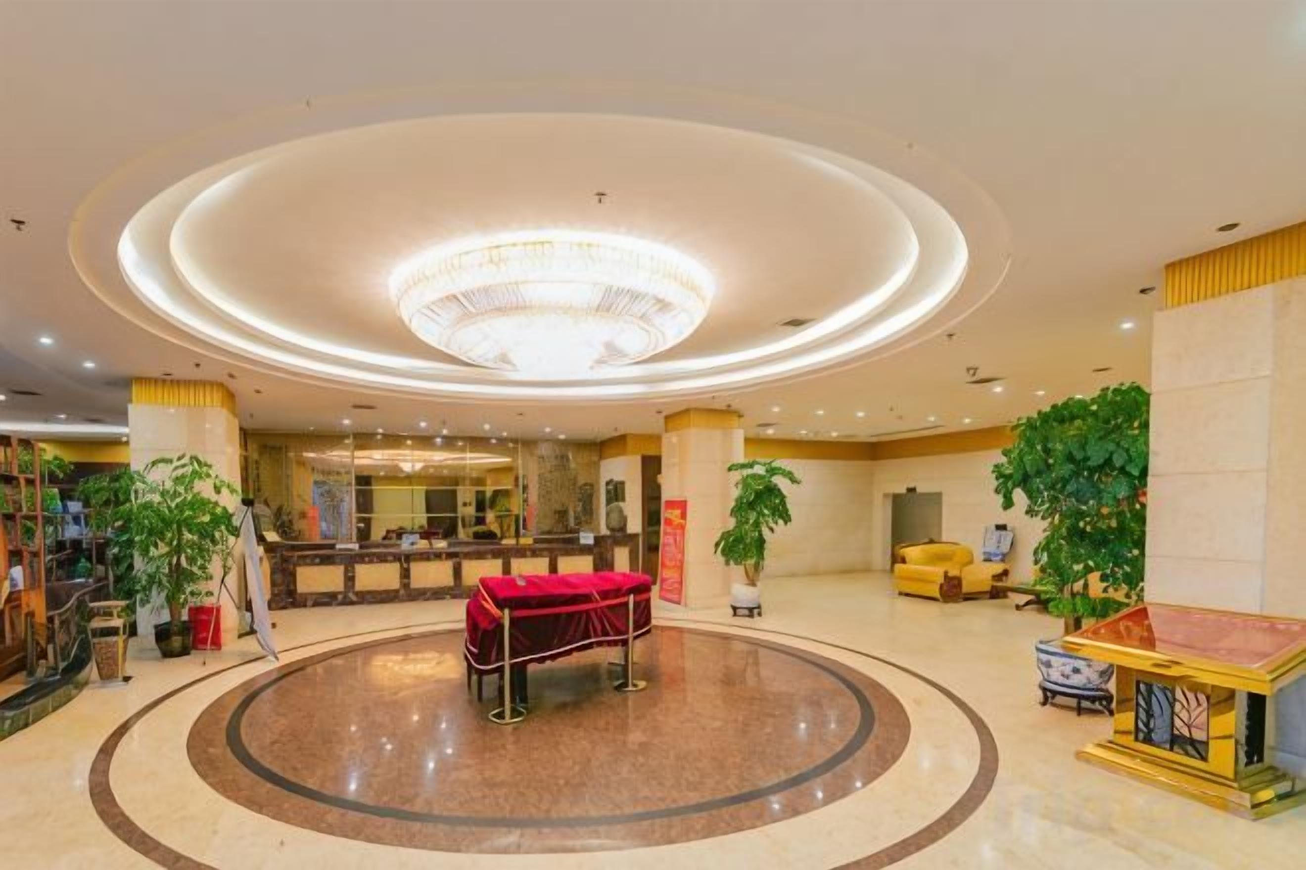 A hotel lobby with a central circular seating area, a reception desk, and potted plants.