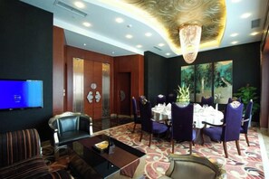 A hotel lobby with a flat-screen TV, a reception desk, and a dining area with chairs and a table. - Xin Shun Hotel (Hongya)