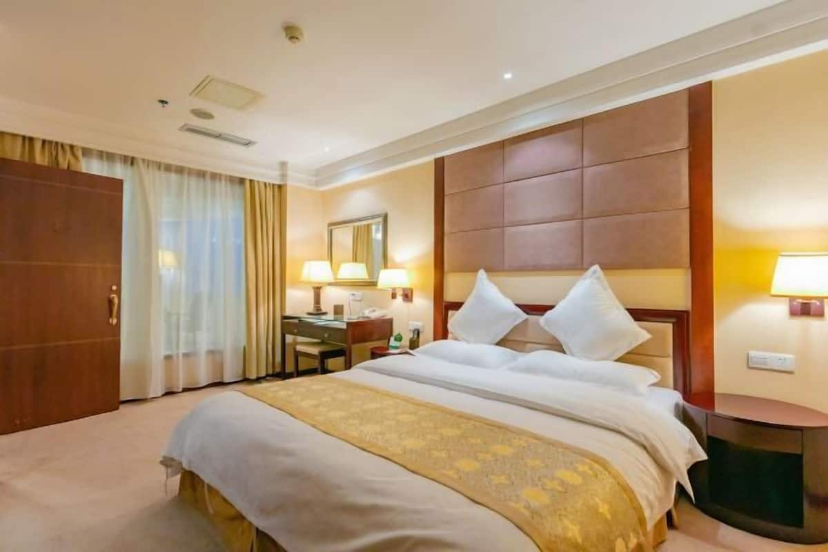 Une chambre d’hôtel avec un grand lit, un bureau, une chaise, un miroir et une table de chevet.