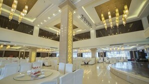 Un amplio vestíbulo de hotel con mesas redondas, sillas blancas y un techo alto con candelabros.