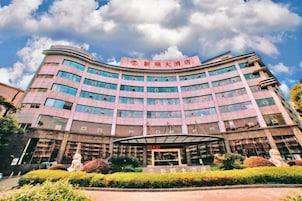 Un hotel de varios pisos con fachada curva, entrada cubierta y jardín frontal ajardinado.