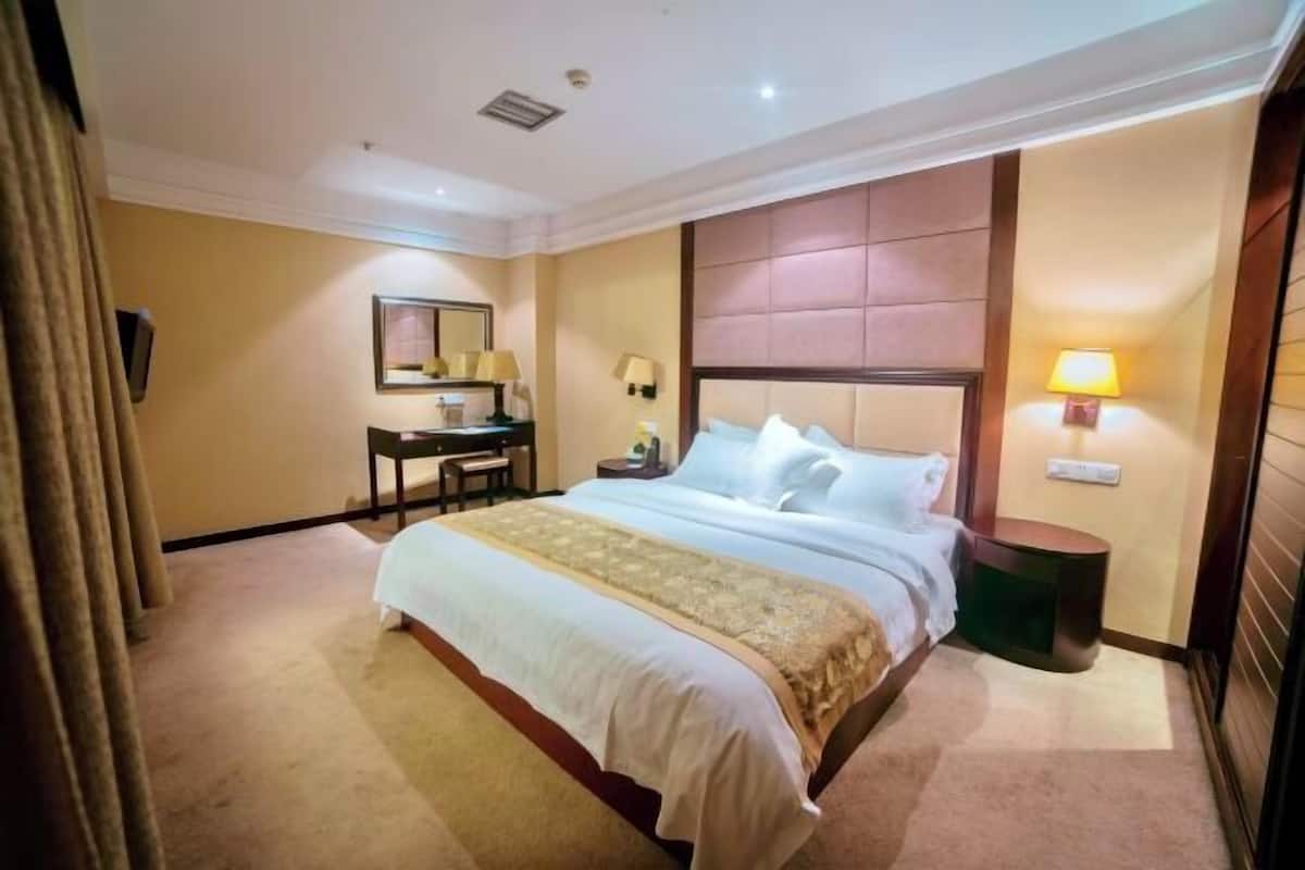 Une chambre d’hôtel avec un grand lit, un bureau, une chaise, un miroir et une table de chevet avec une lampe.