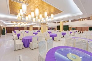 Un salón de banquetes con mesas redondas, sillas blancas y manteles morados.