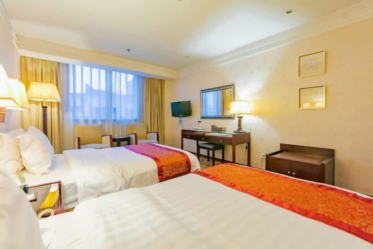 Une chambre d’hôtel avec deux lits, un bureau, une chaise, une télévision et une fenêtre avec des rideaux.