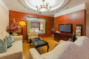 Habitación de hotel con sofá, sillón, mesa de centro, televisión y un jarrón decorativo.