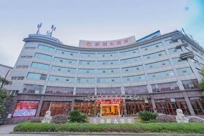 A multi-story hotel with a curved facade, a prominent entrance with a red sign, and a landscaped front garden.