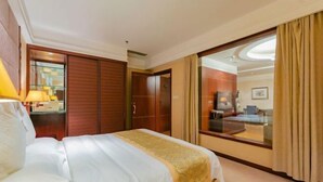 Habitación de hotel con cama, escritorio con lámpara, armario y puerta de cristal corredera que da a un balcón.