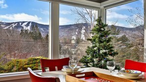 Un comedor con una mesa dispuesta para dos personas, un árbol de Navidad y vistas a la montaña a través de amplias ventanas.