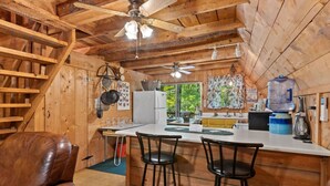 A rustic cabin interior with a wooden interior, a kitchen area with a refrigerator, a sink, and bar stools.