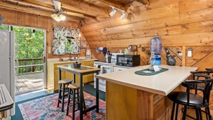 A cabin interior with a wooden interior, a kitchen area with a refrigerator, microwave, and coffee maker, a bar area with stools, and a large water dispenser.