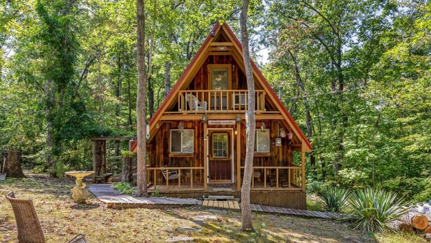 A wooden cabin with a porch, surrounded by trees.