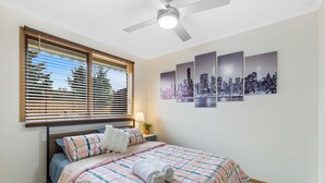 A neatly made bed with a checkered bedspread, a bedside lamp, and a cityscape artwork on the wall.