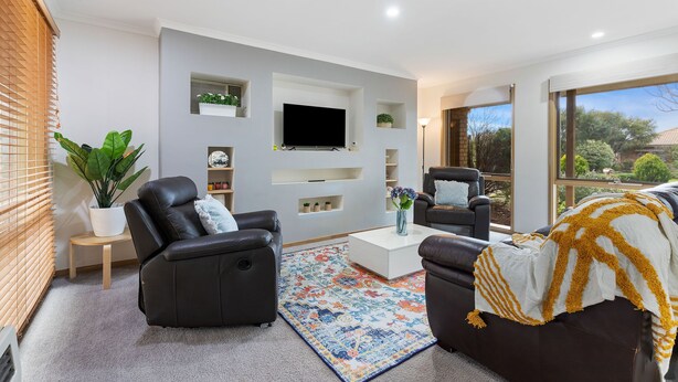 A modern living room with a flat-screen TV, two leather sofas, a coffee table, and a large window offering a view of the outdoors.