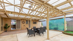 A covered patio with a table and chairs, a brick wall, and a view of a backyard.