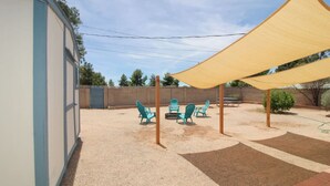 Un espacio al aire libre cubierto con una mesa y sillas, un edificio a la izquierda y una cerca al fondo.