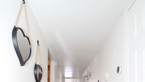 Un estrecho pasillo con paredes blancas y suelo de madera, que conduce a una habitación con un ventanal y una cortina.