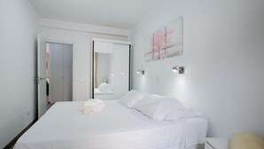 Un dormitorio con cama, mesita de noche, luz de pared y un cuadro.