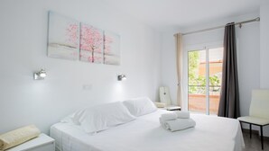 Habitación de hotel con una cama grande, una mesita de noche, una silla y un balcón con cortinas.