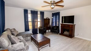 A living room with a sofa, a coffee table, a TV, a fireplace, and a ceiling fan.