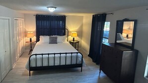 A bedroom with a bed, two bedside tables with lamps, a dresser, a mirror, and a door.