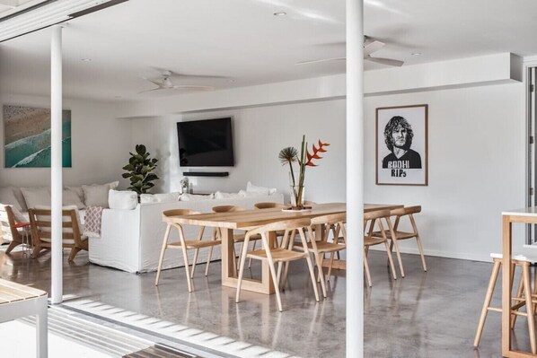 Ein moderner Essbereich mit Holztisch und -stühlen, einer weißen Couch und einem an der Wand befestigten Flachbildfernseher.