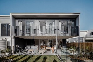 Ein modernes, zweistöckiges Haus mit Balkon, Sitzgelegenheit im Freien und einer sichtbaren Garage.