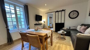 A modern living room with a dining area, a sofa, a TV, and a sliding door. - Gîte with swimming pool, Nordic bath, close to the landing beaches (le manoir)