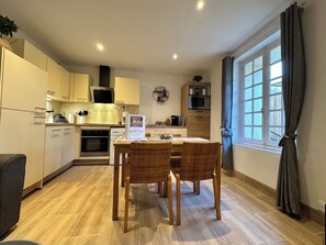 Una cocina moderna con armarios blancos, una mesa de comedor con sillas de mimbre, un microondas y una ventana con cortinas.